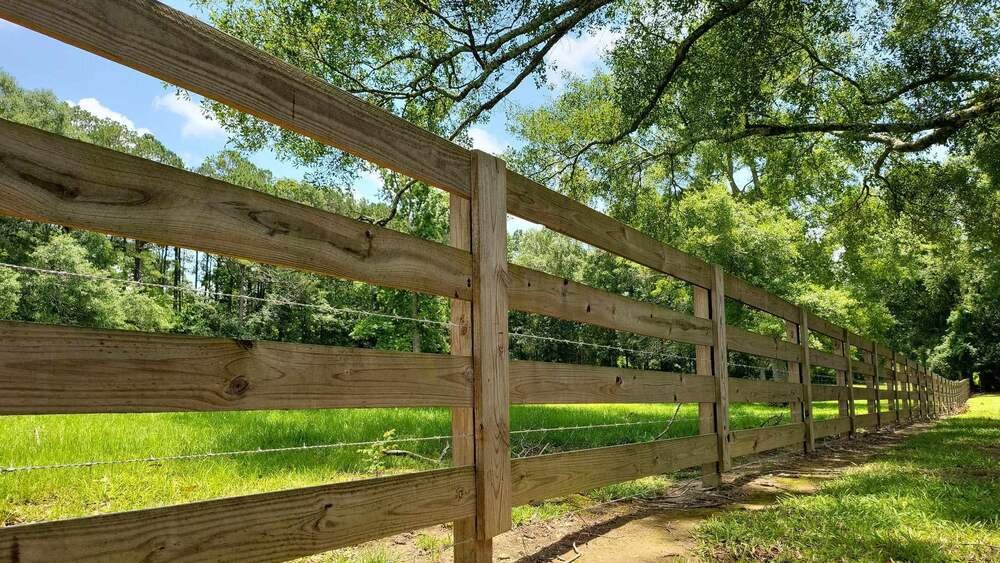 Three-board wood rail fence with wire mesh backing along a green pasture