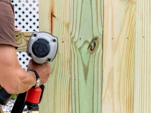 Installer fastening pressure-treated wood pickets with a pneumatic nailer