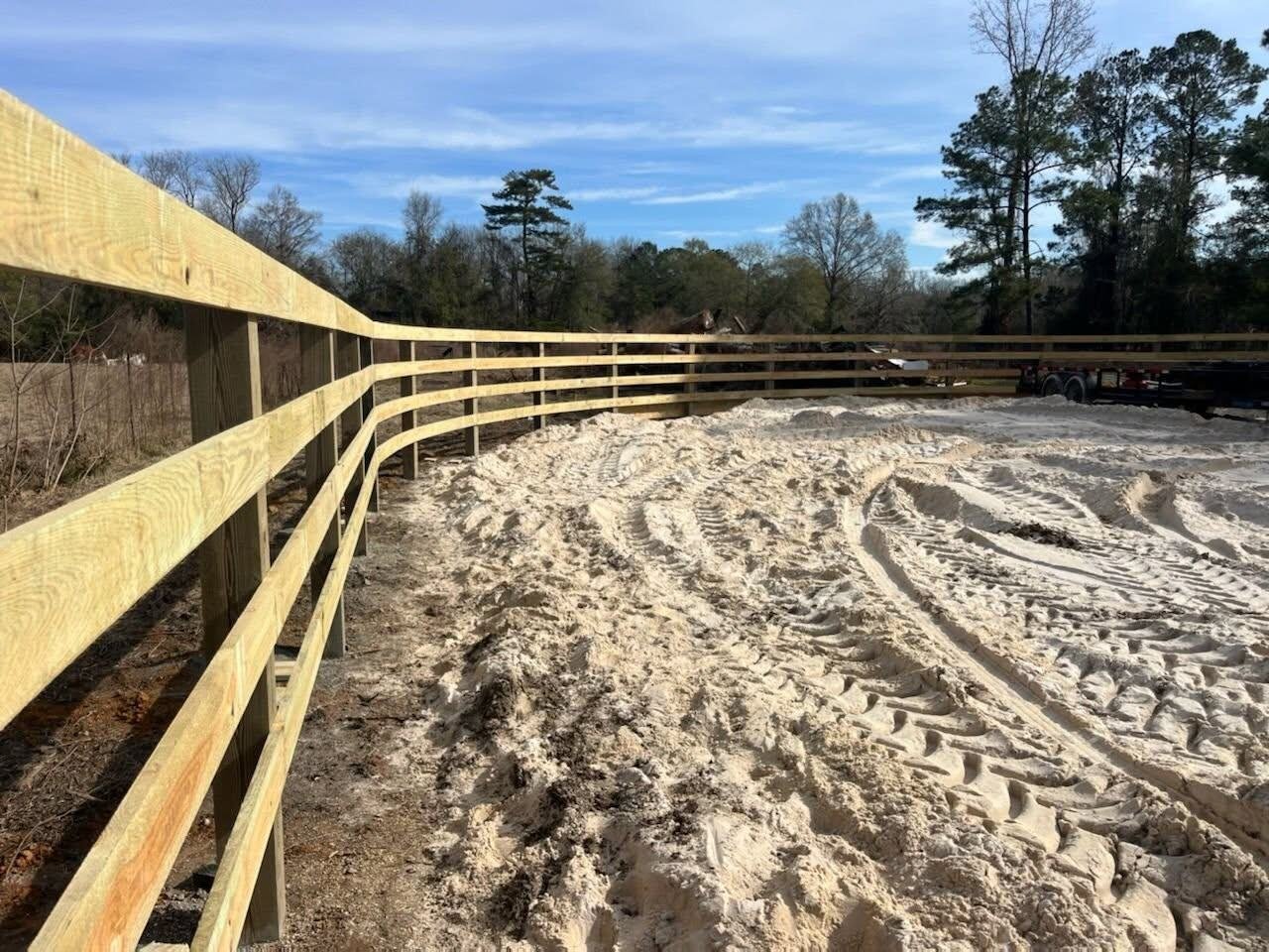 Three-board wood fence enclosing a sand riding arena